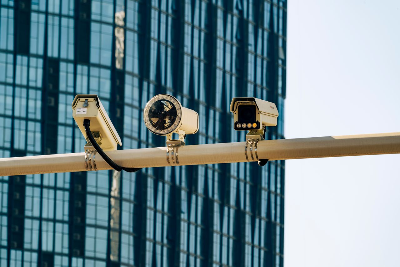 Surveillance cameras mounted on a pole in front of a modern glass building.