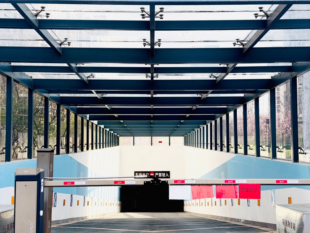 Wide view of a glass-covered entrance leading to an underground parking facility in an urban setting.